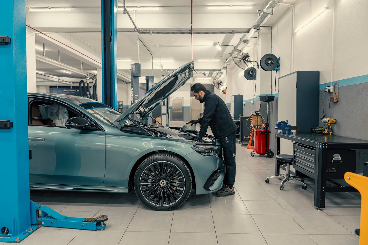 Un mécanicien intervient sous le capot ouvert d’une voiture dans un atelier
