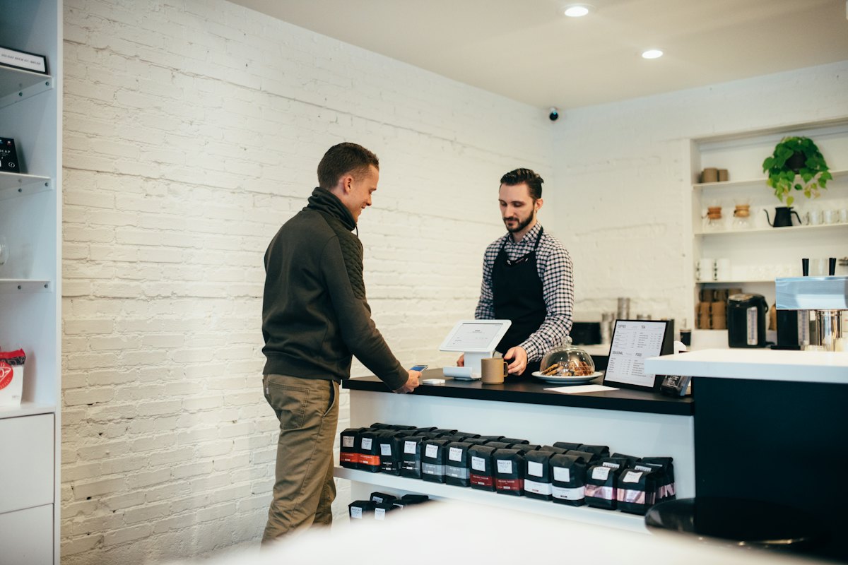 Un commerçant en tablier accueille un client au comptoir de sa boutique